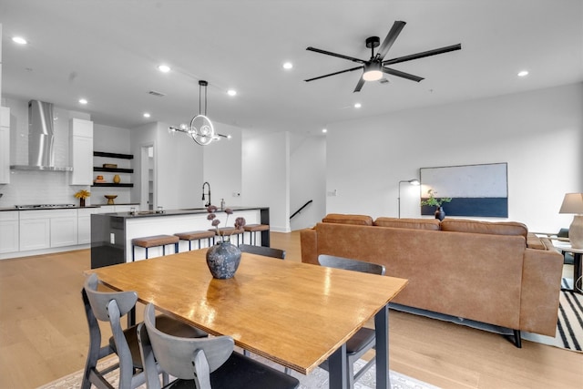 dining space with light hardwood / wood-style floors, sink, and ceiling fan with notable chandelier