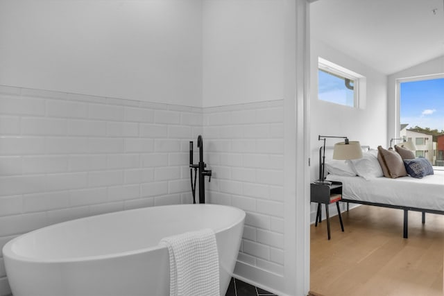 bathroom featuring a bath, hardwood / wood-style flooring, tile walls, and lofted ceiling