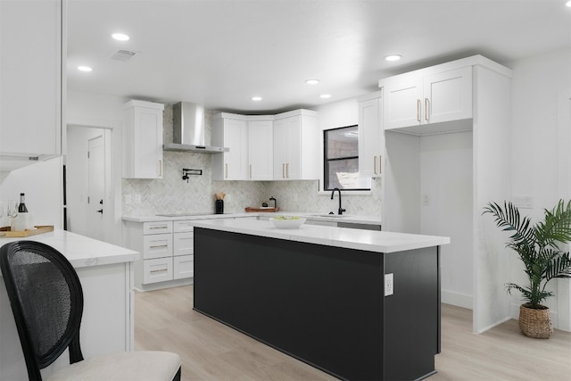 kitchen featuring wall chimney range hood, white cabinetry, light hardwood / wood-style floors, white fridge, and a center island