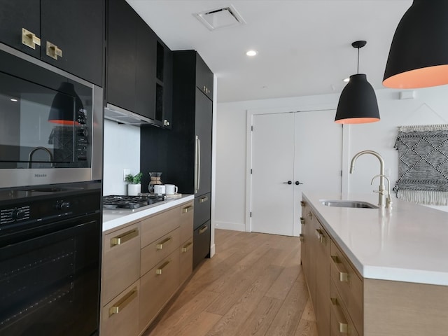 kitchen with oven, a kitchen island with sink, light hardwood / wood-style flooring, pendant lighting, and sink