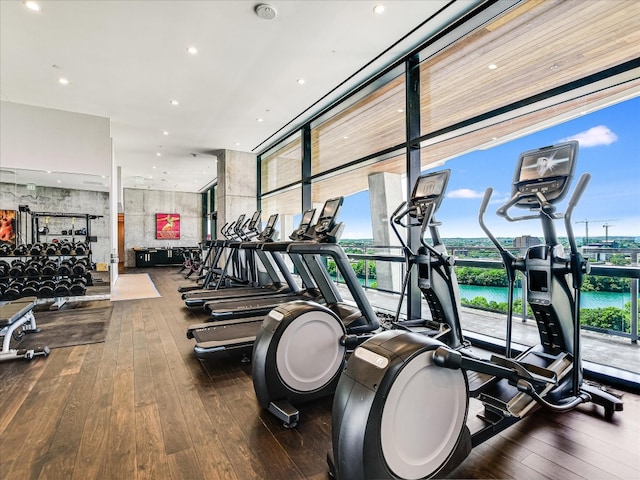 gym with floor to ceiling windows, dark hardwood / wood-style floors, and a water view