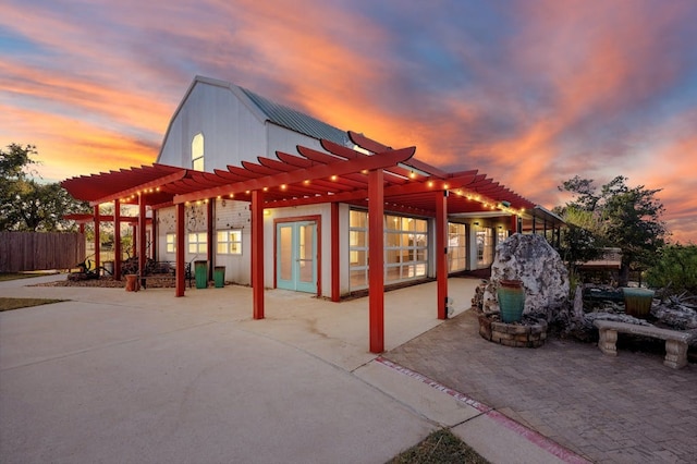 patio terrace at dusk featuring french doors, fence, and a pergola