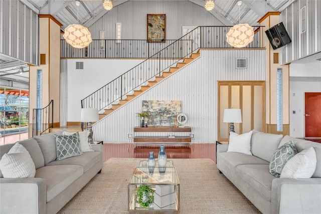 living area featuring high vaulted ceiling, visible vents, and stairway