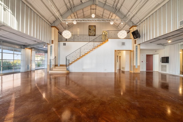 unfurnished living room with high vaulted ceiling, metal wall, and stairs