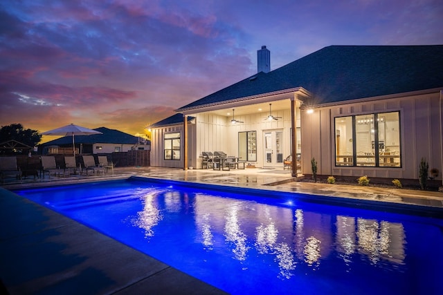 pool at dusk with ceiling fan, fence, a patio, outdoor dining area, and an outdoor pool