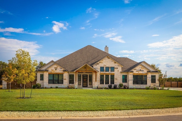 view of front of property featuring a front yard, a chimney, a shingled roof, and stone siding