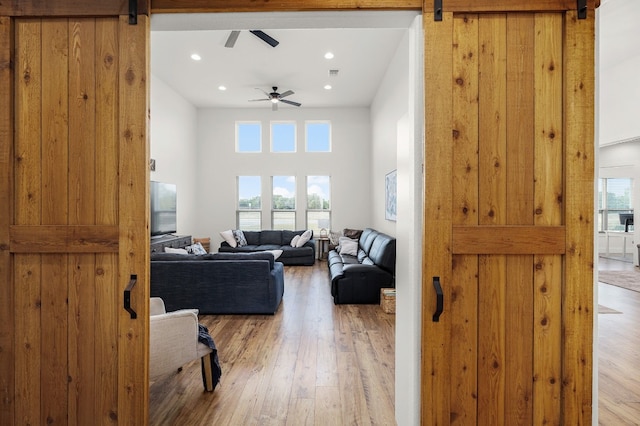 living room with ceiling fan, a high ceiling, light wood-type flooring, and a barn door