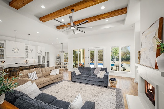 living room with beamed ceiling, french doors, light wood-type flooring, and a high ceiling