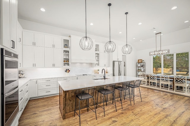 kitchen with stainless steel appliances, a center island with sink, sink, white cabinetry, and light hardwood / wood-style floors