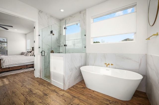 bathroom with ceiling fan, tile walls, wood-type flooring, and plus walk in shower