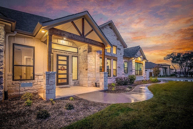 property entrance with a lawn, a shingled roof, and stone siding