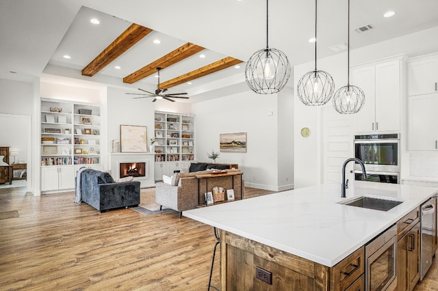 kitchen with white cabinets, hanging light fixtures, a kitchen island with sink, built in shelves, and stainless steel appliances