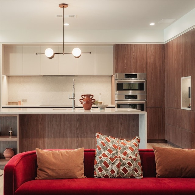 kitchen featuring white cabinetry, decorative light fixtures, and stainless steel double oven