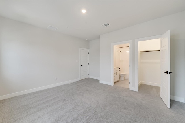 unfurnished bedroom with a walk in closet, ensuite bathroom, a closet, and light colored carpet