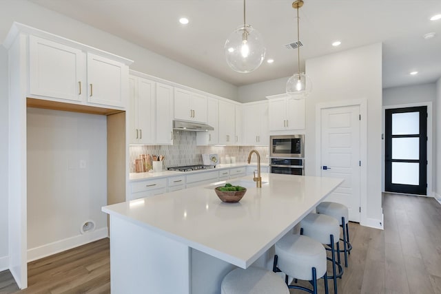 kitchen with white cabinetry, a kitchen island with sink, hanging light fixtures, stainless steel appliances, and decorative backsplash