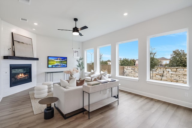 living room featuring a fireplace, wood-type flooring, ceiling fan, and a healthy amount of sunlight