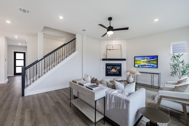 living room featuring dark hardwood / wood-style flooring, a large fireplace, and ceiling fan