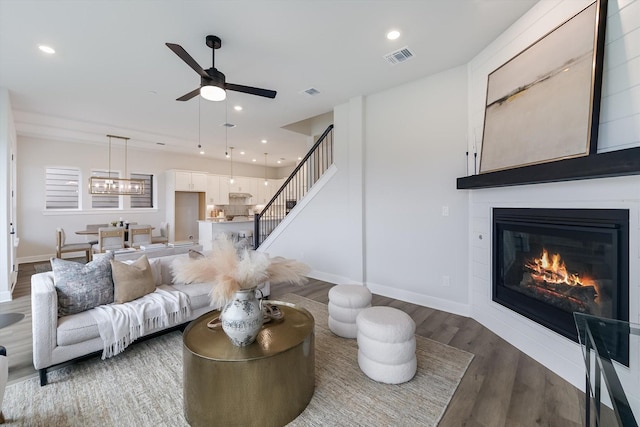 living room featuring a fireplace, ceiling fan, and dark wood-type flooring