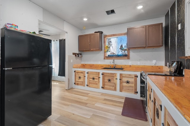 kitchen featuring black fridge, wood counters, light wood-type flooring, electric stove, and sink