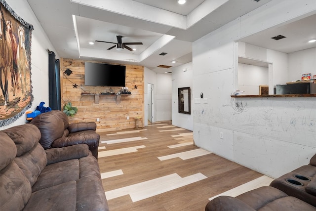 living room with wood walls, a tray ceiling, light wood-type flooring, and ceiling fan