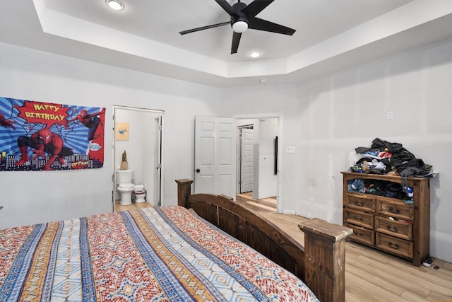 bedroom with ensuite bath, a tray ceiling, light hardwood / wood-style flooring, and ceiling fan