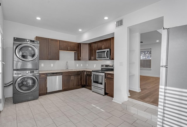 kitchen featuring tasteful backsplash, dark brown cabinets, light wood-type flooring, stainless steel appliances, and stacked washer and clothes dryer