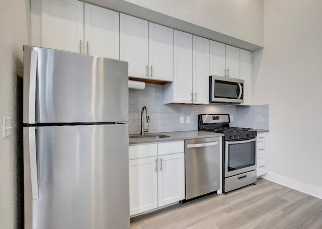 kitchen featuring backsplash, appliances with stainless steel finishes, white cabinetry, light hardwood / wood-style flooring, and sink