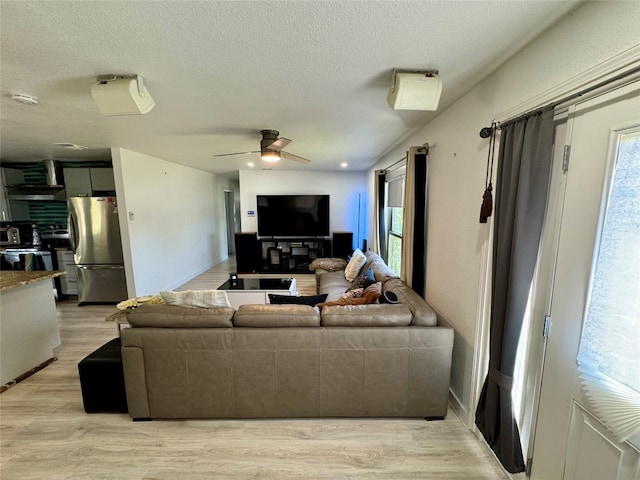 living room with a textured ceiling, light wood-type flooring, and ceiling fan