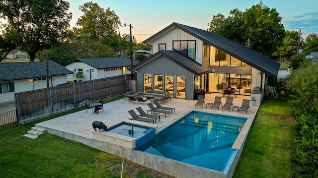 back house at dusk with a yard, a patio area, a swimming pool with hot tub, and an outdoor living space with a fire pit