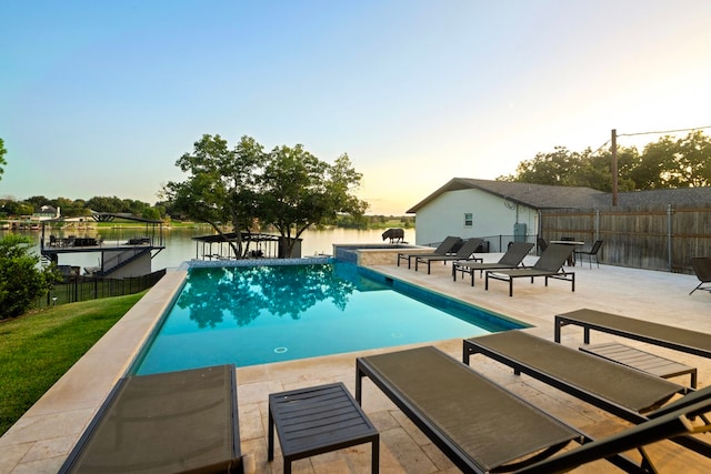 pool at dusk featuring a water view and a patio