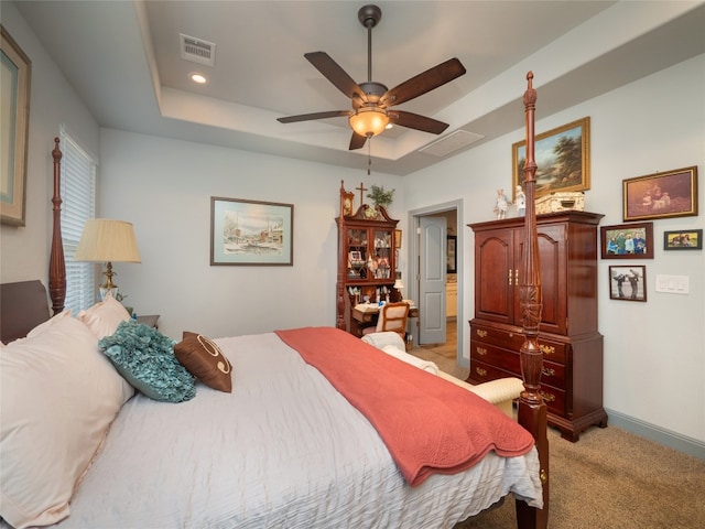 bedroom with light colored carpet, a raised ceiling, and ceiling fan