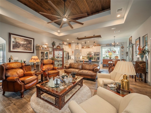 living room with wooden ceiling, hardwood / wood-style flooring, ceiling fan with notable chandelier, and a raised ceiling