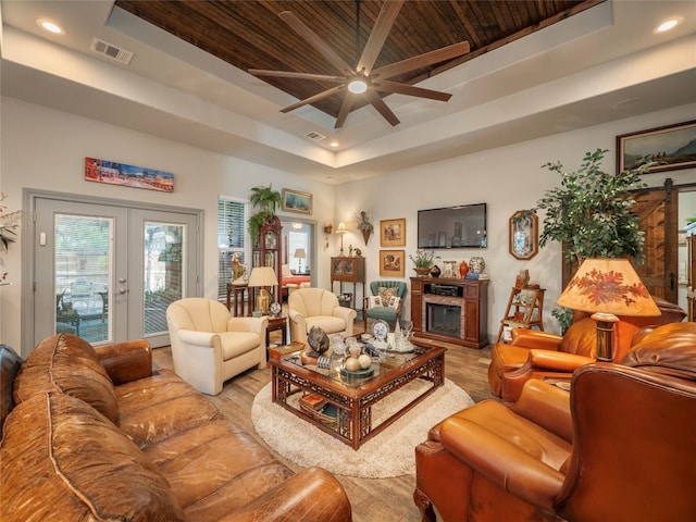 living room featuring ceiling fan, a raised ceiling, a barn door, wooden ceiling, and french doors