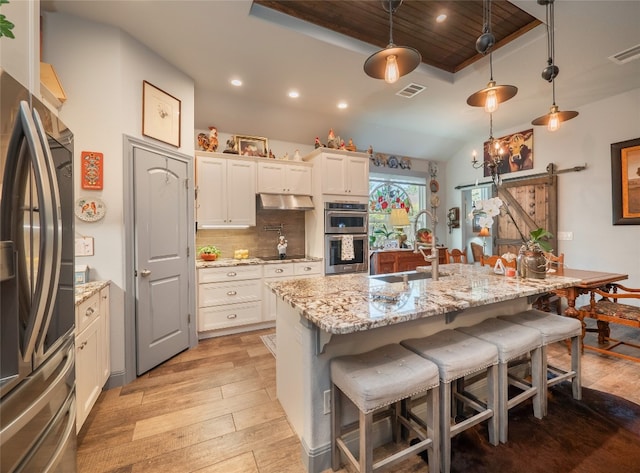 kitchen featuring a barn door, light hardwood / wood-style floors, stainless steel appliances, decorative light fixtures, and a kitchen island with sink