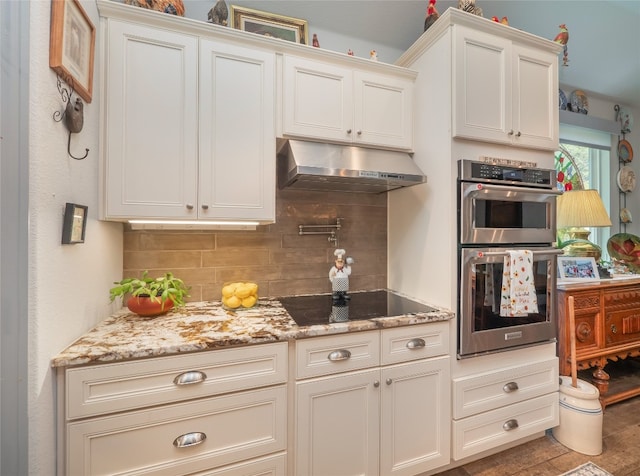 kitchen with backsplash, black electric cooktop, stainless steel double oven, white cabinets, and light stone counters