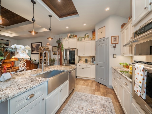 kitchen featuring white cabinets, stainless steel appliances, decorative light fixtures, and a raised ceiling