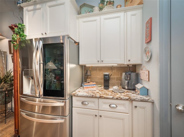 kitchen featuring stainless steel fridge, white cabinets, backsplash, light stone countertops, and wood-type flooring