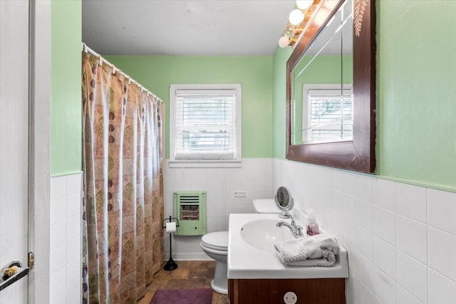 bathroom featuring heating unit, vanity, tile walls, and toilet