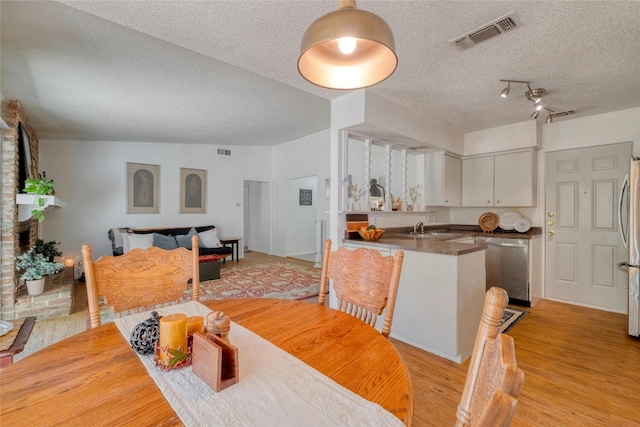 dining area with sink, light hardwood / wood-style flooring, a textured ceiling, and lofted ceiling