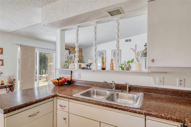 kitchen with sink, vaulted ceiling, kitchen peninsula, and a textured ceiling