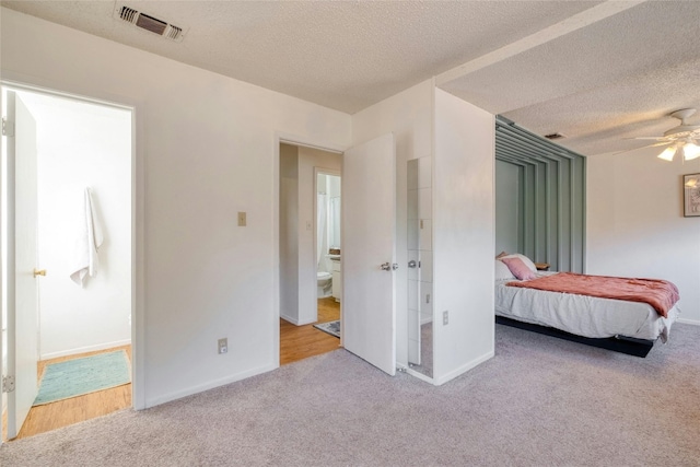 bedroom featuring light carpet, a textured ceiling, ensuite bath, and ceiling fan