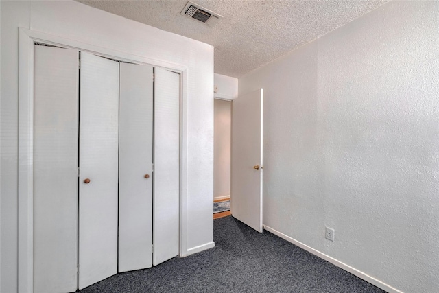 unfurnished bedroom featuring dark carpet, a textured ceiling, and a closet