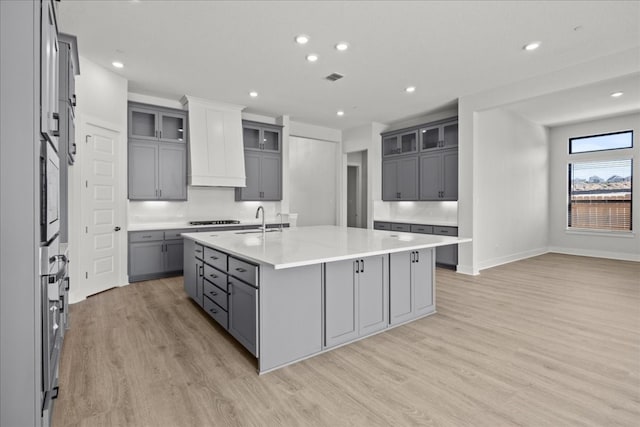 kitchen featuring gray cabinetry, sink, cooktop, light hardwood / wood-style flooring, and a center island with sink