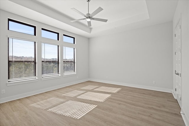 empty room with light wood-type flooring, a raised ceiling, and ceiling fan