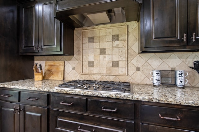 kitchen featuring light stone countertops, stainless steel gas stovetop, decorative backsplash, dark brown cabinets, and custom exhaust hood