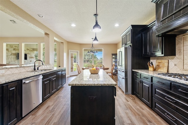 kitchen with appliances with stainless steel finishes, backsplash, custom exhaust hood, a kitchen island, and hanging light fixtures