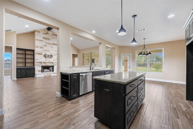 kitchen featuring sink, stainless steel dishwasher, a fireplace, decorative light fixtures, and a kitchen island