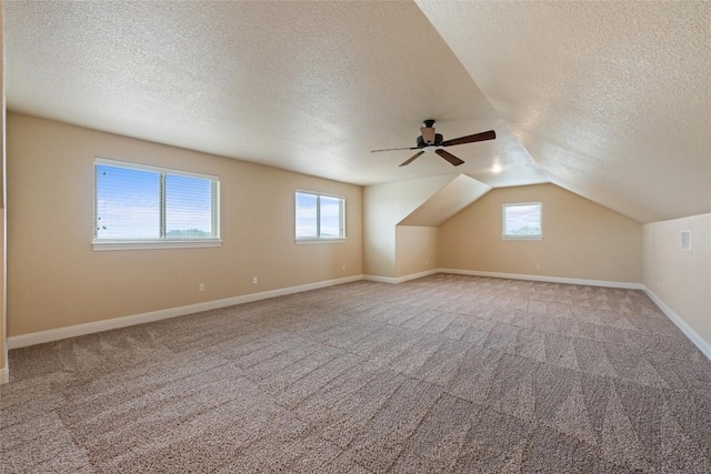 additional living space with light carpet, a textured ceiling, lofted ceiling, and baseboards