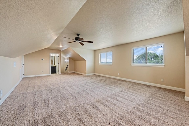 bonus room with baseboards, light colored carpet, lofted ceiling, ceiling fan, and a textured ceiling