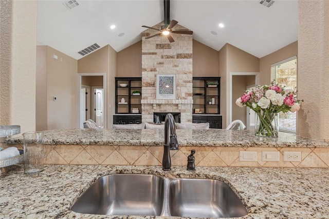 kitchen with light stone counters, visible vents, a sink, and a stone fireplace